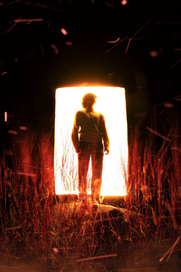 Silhouette of a person in front of an illuminated portal surrounded by darkness.