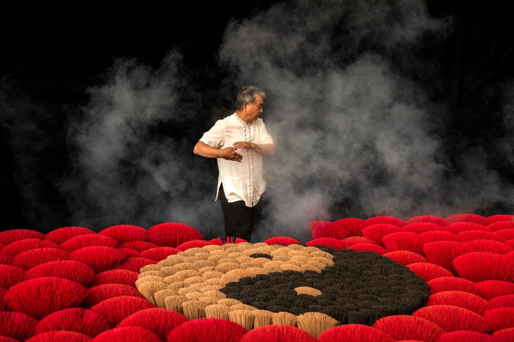 Man standing among colorful incense sticks with smoke in a Taiwan ceremony.